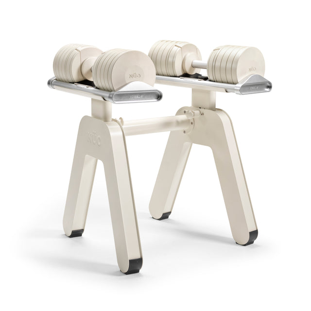 A pair of NÜOBELL-S adjustable dumbbells rest on the Bells of Steel USA NÜOBELL-S Floor Stand, which features four legs with black feet, all set against a plain white background.