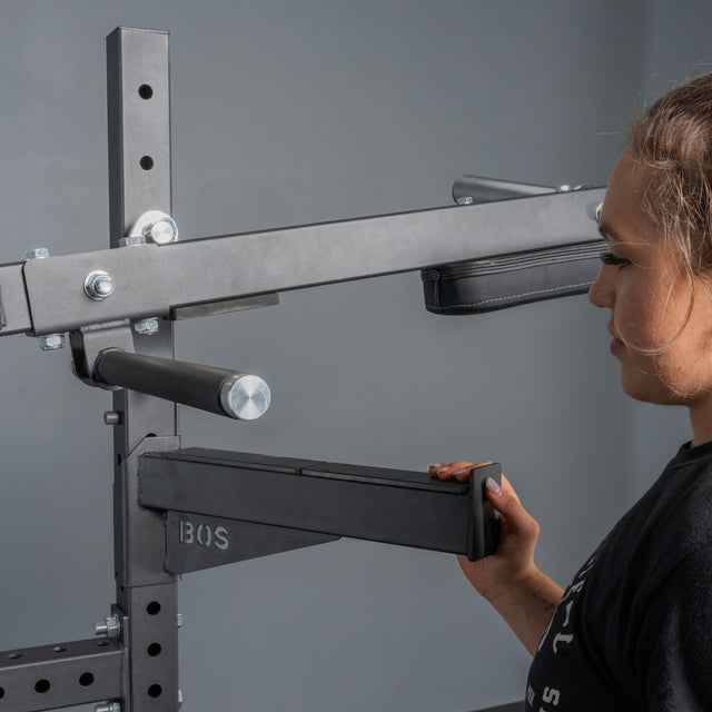 A person adjusts the arm of the Pandemonium Squat – 3-in-1 Pendulum Squat / Calf Press / Viking Press Machine by Bells of Steel USA, with a focus on the equipment and their hand against a plain gray background.