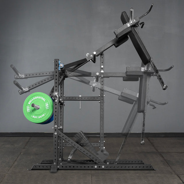 The Bells of Steel USA Pandemonium Squat – a 3-in-1 Pendulum Squat, Calf Press, and Viking Press Machine – is shown in black with padded supports, a green weight plate, and set against a gray wall and floor.