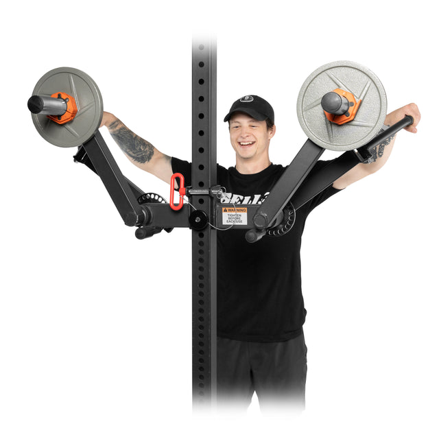 A person uses the Bells of Steel Shoulder Boulder/Chest Fly Attachment, lifting two weighted arms on a black machine with orange and silver accents, smiling as they raise both arms outward.