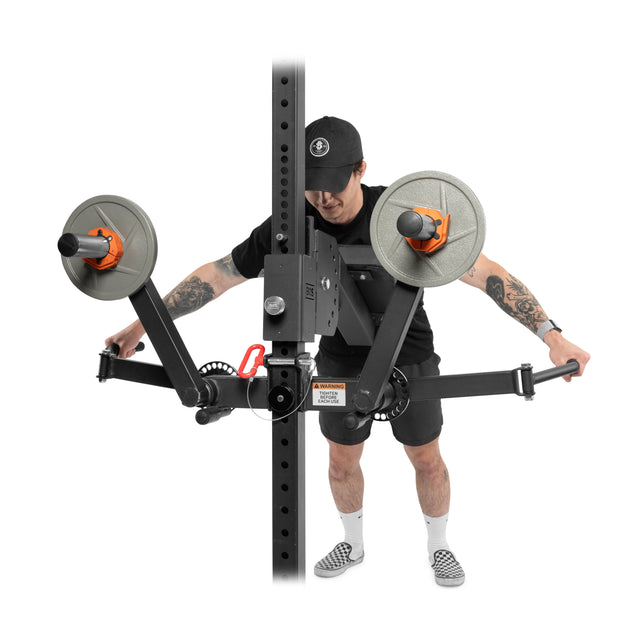 Wearing black athletic clothing and a hat, a person uses the Bells of Steel Shoulder Boulder/Chest Fly Attachment with both arms extended outward, performing chest fly exercises on the machine.