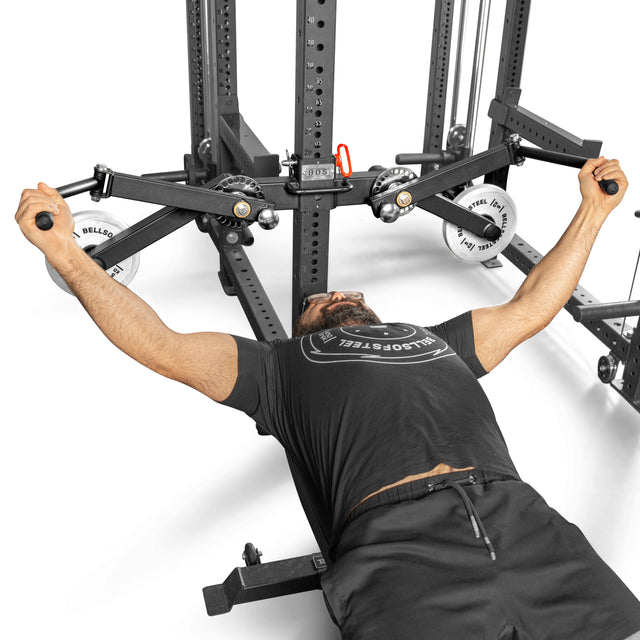 A person uses the Bells of Steel Shoulder Boulder/Chest Fly Attachment, a black, space-saving fitness accessory with adjustable weights and pulleys—ideal for chest fly and shoulder workouts.