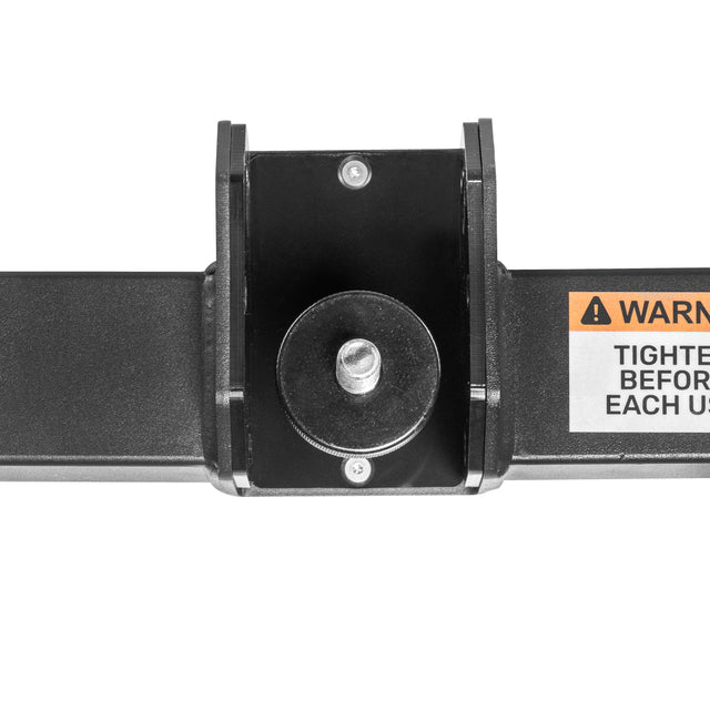Close-up of the Bells of Steel Shoulder Boulder/Chest Fly Attachment—a black metal bracket with a central bolt, mounted on a rectangular bar. Part of compact gym gear, a partial warning label hints at its space-saving fitness design.