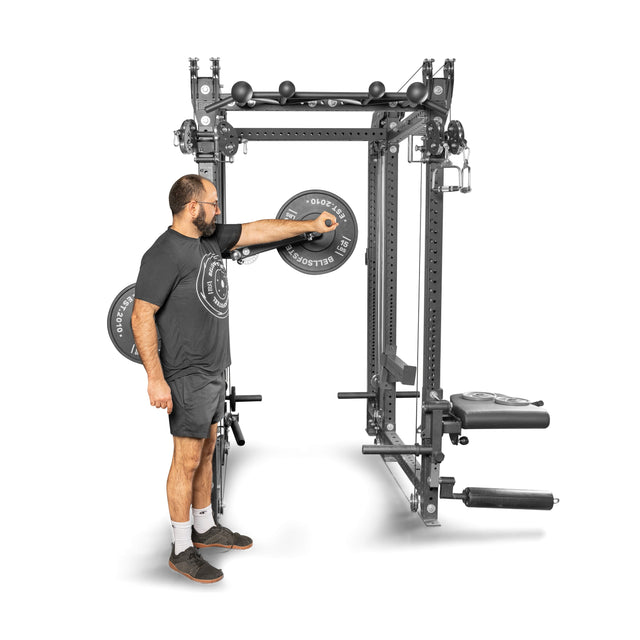A man in athletic wear adjusts the Bells of Steel Shoulder Boulder/Chest Fly Attachment on a multifunctional power rack, showing this space-saving, versatile gym equipment on a white background.