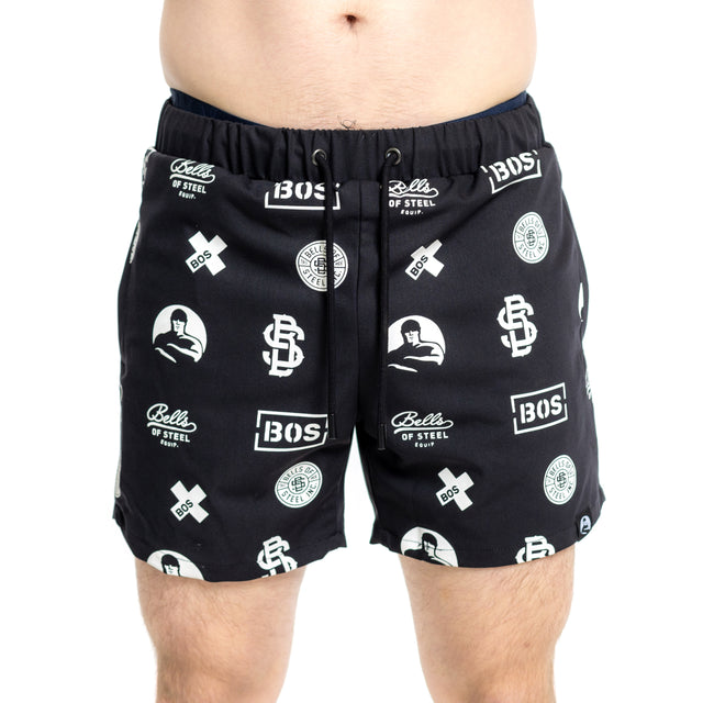 A person wearing Bells of Steel Gym Shorts in black, made from stretchy lightweight fabric and featuring white "Bells of Steel" and "BOS" logos, stands against a plain white background.