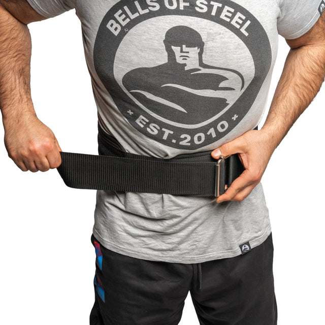 Wearing a Bells of Steel T-shirt, someone fastens the Bells of Steel Self Locking Belt around their waist for added back support before exercising.