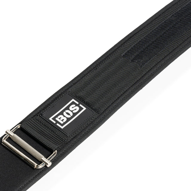 Close-up of the Bells of Steel Self Locking Belt featuring a black adjustable strap, metal buckle, reinforced stitching, and a rectangular BOS logo patch on the fabric.