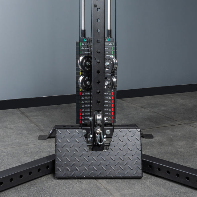 Close-up of a Bells of Steel All-in-One Trainer weight stack with labeled plates and adjustment pin on a black frame, set on gray tiles against a gray wall—ideal for any home gym.