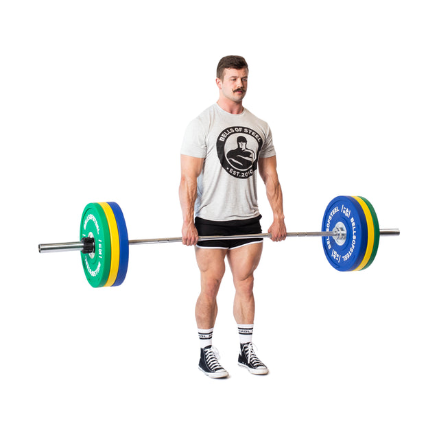 A man in a gray t-shirt and black shorts lifts a barbell with Bells of Steel Urethane Bumper Plates, holding it at thigh level against a white background.