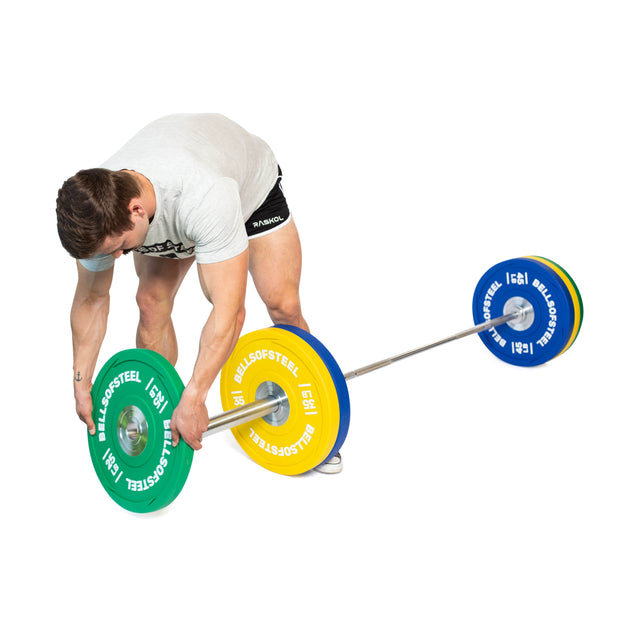 Wearing athletic gear, a person adjusts green and yellow Bells of Steel Urethane Bumper Plates on a barbell, while another barbell with blue plates sits nearby against a white background.