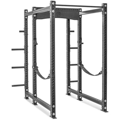A large, sturdy, black metal power rack with multiple holes for adjustable attachments, safety straps, and weight storage pegs on both sides, designed for weightlifting exercises.