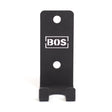 Bells of Steel Hanging Barbell Holders: black metal wall hooks with two mounting holes, designed for secure barbell storage. "BOS" logo in a white rectangle on the front, shown against a white background.