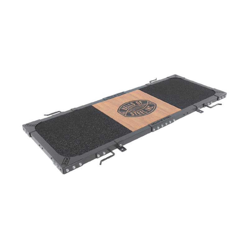 A rectangular weightlifting platform by Bells of Steel with a black grip surface, metal edges, and a wooden center panel featuring the "HEROES OF STEEL USA" logo—built durable for your active home gym.