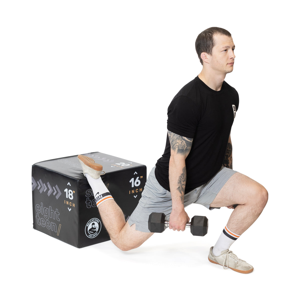 A man in a black t-shirt and gray shorts performs a Bulgarian split squat using the Bells of Steel Foam Soft Plyo Box (16 x 18 x 20) for support, lunging forward with one leg while the other rests on the box, holding a dumbbell in each hand, demonstrating versatile home gym exercises.