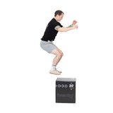 In athletic wear, a person jumps onto a 20-inch Foam Soft Plyo Box by Bells of Steel. Mid-air with bent knees and arms forward, the white background highlights this fitness activity, showcasing agility using versatile gym equipment.