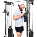 A bearded man with short hair exercises using the Bells of Steel Cable Tower Squat Stands, emulating a sleek home gym setup. In a gray T-shirt and black shorts, he stands against a white background, showcasing focus and strength with the cable-driven lat pulldown machine.