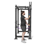A man in a black t-shirt and shorts adjusts a colorful bar on a black power rack featuring Bells of Steel Hanging Barbell Holders in a gym.