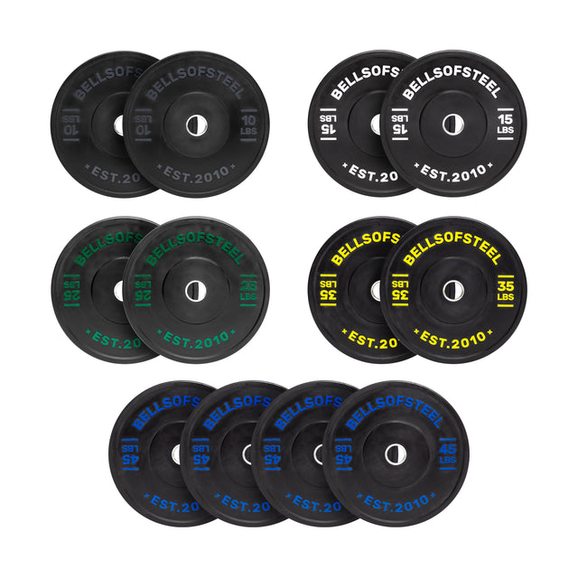 The Dead Bounce Conflict Bumper Plates by Bells of Steel are arranged in rows with weights from 10 to 45 pounds. Each black plate features colored text indicating weight—white, green, yellow, or blue. A stainless steel insert ensures durability and "Bells of Steel" is boldly printed on each plate.