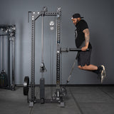 A man in athletic wear and a cap performs dips on parallel bars attached to the Bells of Steel USA Oblivyon Tower - 3" x 3” Cable Tower in a gym.