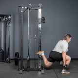 Wearing athletic gear, a person does a Bulgarian split squat with a dumbbell, placing one foot on the Bells of Steel USA Oblivyon Tower - 3" x 3” Cable Tower in the gym.