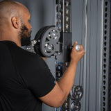 A man in a black shirt adjusts a pulley on the Bells of Steel USA Oblivyon Tower – 3" x 3” Cable Tower, turning a handle to secure or move the home gym cable machine.