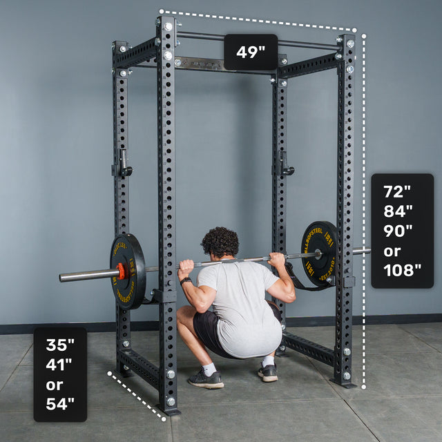 A person performs a barbell squat inside the Bells of Steel Manticore Four Post Power Rack Builder (3" x 3", 1" Holes), a sturdy black power rack featuring a 4-post design. Displayed dimensions are 49" width, depths of 35", 41", or 54", and height options including 72", 84", 90", or 108". This versatile home gym power rack stands against a gray background.