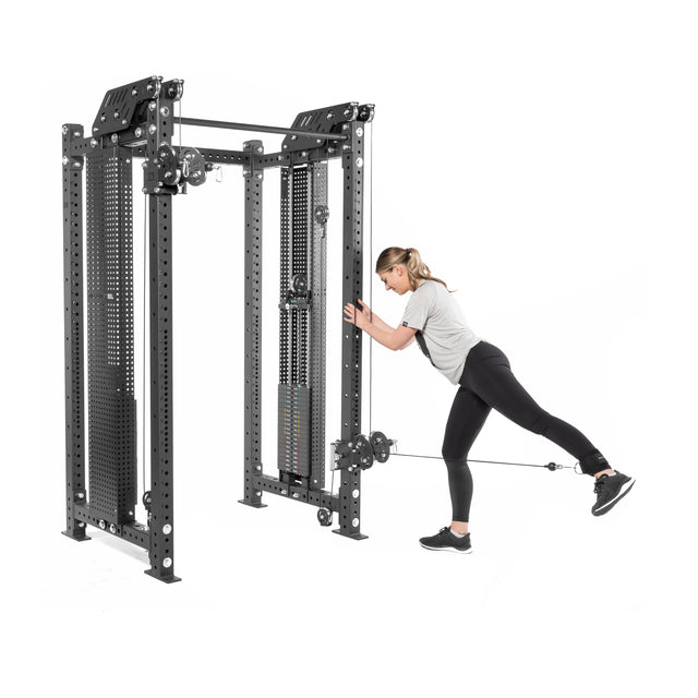 A person in athletic wear uses the Bells of Steel Kraken Rack Attachment for 4 Post Hydra & Manticore Racks for a standing leg exercise. Leaning slightly forward, they extend one leg behind with the cable attached to their ankle, enjoying a versatile and streamlined workout with adjustable weights.