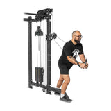 A person in a black t-shirt, shorts, and glasses exercises with the Bells of Steel Kraken Rack Attachment for 4 Post Hydra & Manticore Racks (Single Side), pulling cables forward while standing. The machine's adjustable trolleys accommodate versatile workouts with its weights.