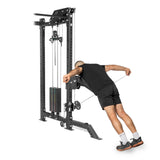 Dressed in black, a person leans forward, gripping the cables of the Kraken Rack Attachment for 4 Post Hydra & Manticore Racks by Bells of Steel. The tall machine features adjustable weights and trolleys for a versatile workout against the white background.