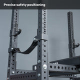 Close-up of the Bells of Steel USA Hydra Four Post Converter Bench, featuring black metal construction with numbered holes and attached safety straps for precise bench press safety. Plain gray background with text: "Precise safety positioning.