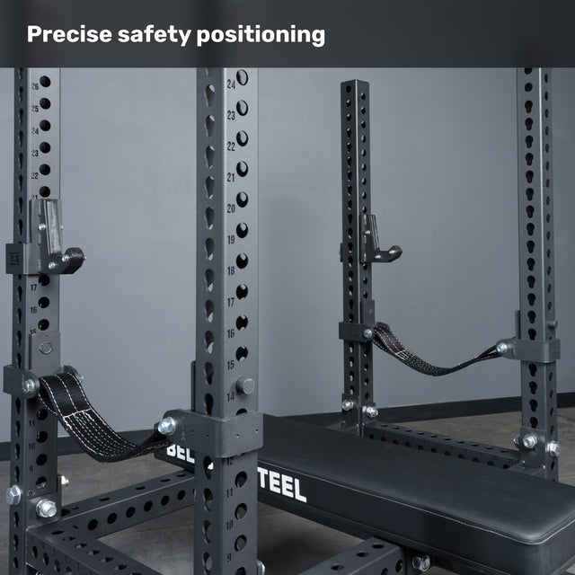 A close-up of the Bells of Steel USA Manticore Four Post Converter Bench, featuring adjustable safety straps and numbered holes. Text at the top reads, “Precise safety positioning.”.