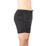 A person in Bells of Steel Gym Shorts stands against a white background. Made from high-performance polyester, these black shorts offer optimal comfort with an adjustable drawstring and stretchy fabric.