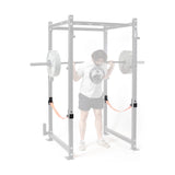 A person squats inside a power rack, using Bells of Steel Safety Strap Connectors. The highlighted connectors emphasize training safety, while the rest of the rack is faded for focus.