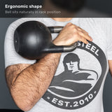 A person holds the Bells of Steel 6-12KG Adjustable Kettlebell in rack position against their chest. Their shirt displays a strongman logo with “STEEL EST. 2010”. Text above reads, “Ergonomic shape: Bell sits naturally in rack position.”.