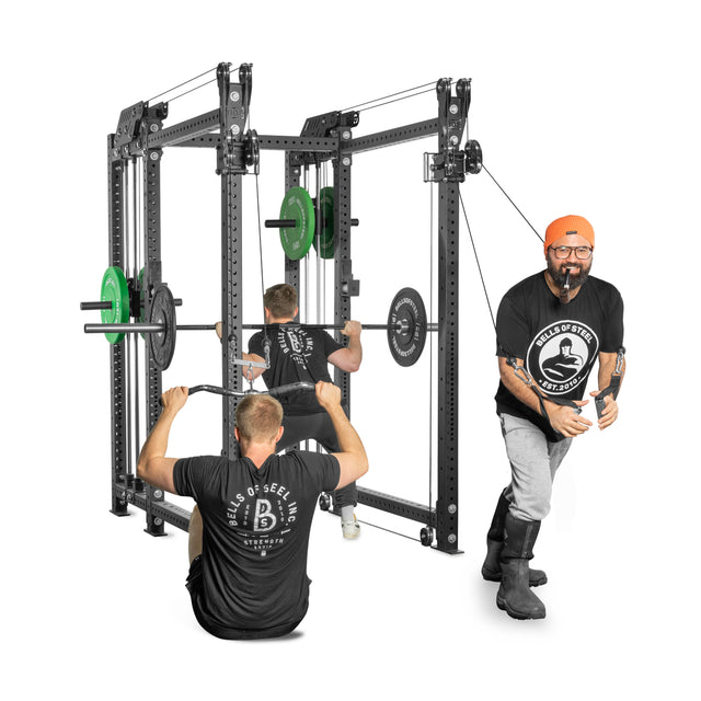 Three people demonstrate workouts using a Kraken Rack Attachment for 6 Post Hydra Racks by Bells of Steel. One squats with a barbell, another performs seated lat pulldowns with the dual-handle cable tower, and the third uses resistance bands—all wearing branded gym shirts.