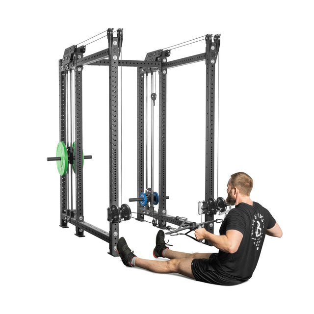 A person with short hair uses the Bells of Steel Kraken Rack Attachment, a compact cable system for rowing exercises with dual handles, pulleys, cables, and weight plates on a white background.