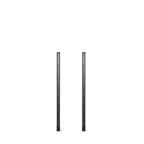 Two tall, black metal Manticore Vertical Uprights by Bells of Steel stand parallel on a white background, featuring evenly spaced holes for compatibility with various rack attachments.