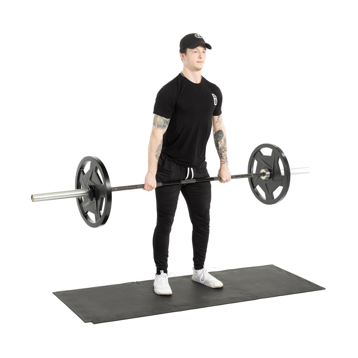 A person dressed in black performs a barbell lift on Bells of Steel 24" x 24" Puzzle Mats, providing floor protection and creating a sleek commercial gym aesthetic against the white background.