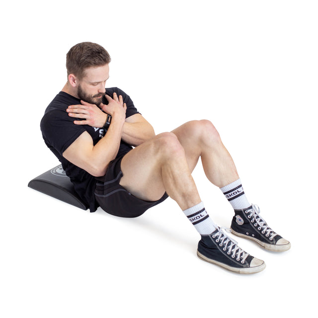 A man is doing sit-ups on a Bells of Steel Sit Up Mat, ensuring great lumbar support. He's in a black t-shirt, black shorts, white socks, and black high-top sneakers with his arms crossed over his chest, looking focused.