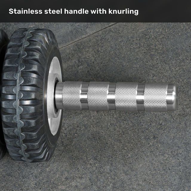 Close-up of the ABsyidyan Stainless Steel Ab Roller by Bells of Steel USA, featuring a knurled stainless steel handle and extra-wide dual wheels on a textured gray surface. Text above: "Stainless steel handle with knurling.