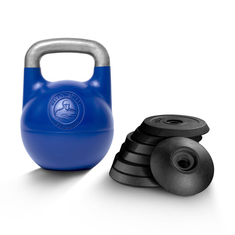 A Bells of Steel Adjustable Competition Kettlebell with a silver handle sits beside black weight plates against a white background. The kettlebell features a strongman logo on its front.