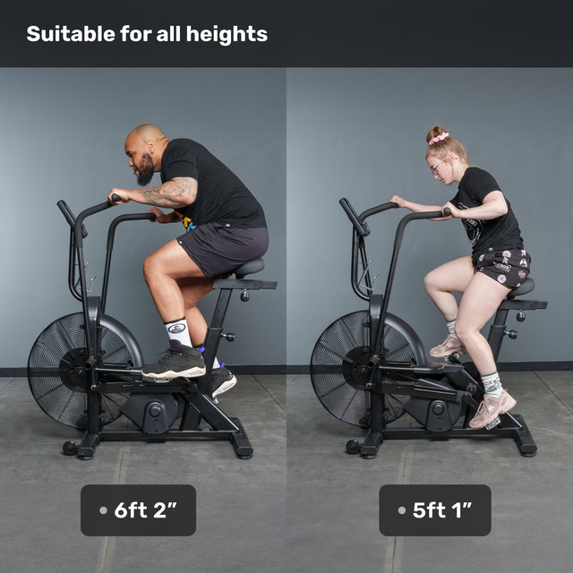 Two people, 6'2" and 5'1", ride Bells of Steel Residential Air Bikes with Wind Guard side by side at home. Text reads "Suitable for all heights." Both look comfortable and well-positioned on the bikes.