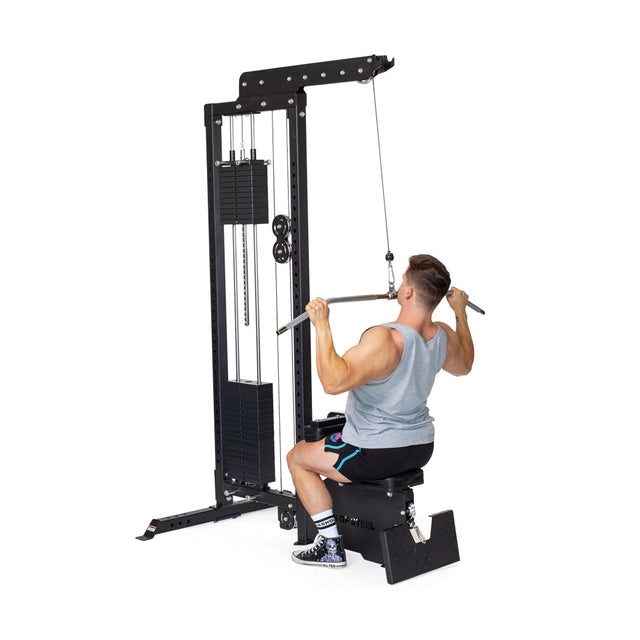 Seated on a sleek black workout machine, a person in athletic clothing grips the Bells of Steel Lat Pulldown Bar with rubberized grips and uses a rotating connection point to perform smooth exercises, supported by the vertical weight stack.