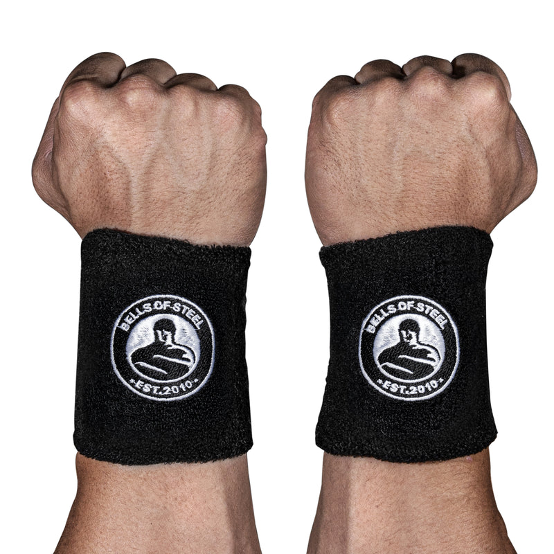 Two fists with wrists facing forward, each wearing Bells of Steel BellGuard Kettlebell Wrist Guards—black guards bearing a circular kettlebell logo and "EST. 2010" in white—essential workout accessories.