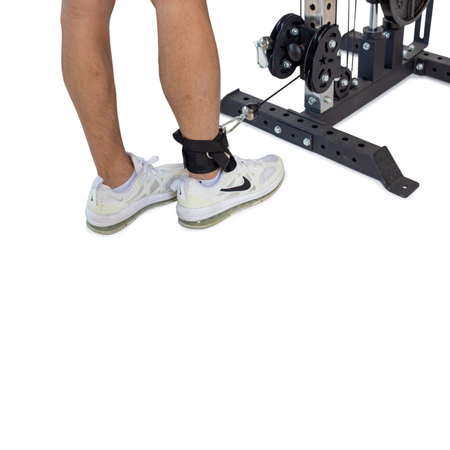 A person wearing white sneakers with Bells of Steel Adjustable Ankle Strap Cable Attachments is prepping for intense glute-training exercises against a plain white background.