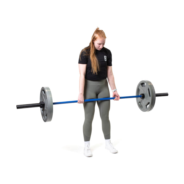 A person with long hair is powerlifting the Bells of Steel Multi-Purpose Olympic Barbell while wearing a black shirt, green leggings, and white sneakers against a plain white background.