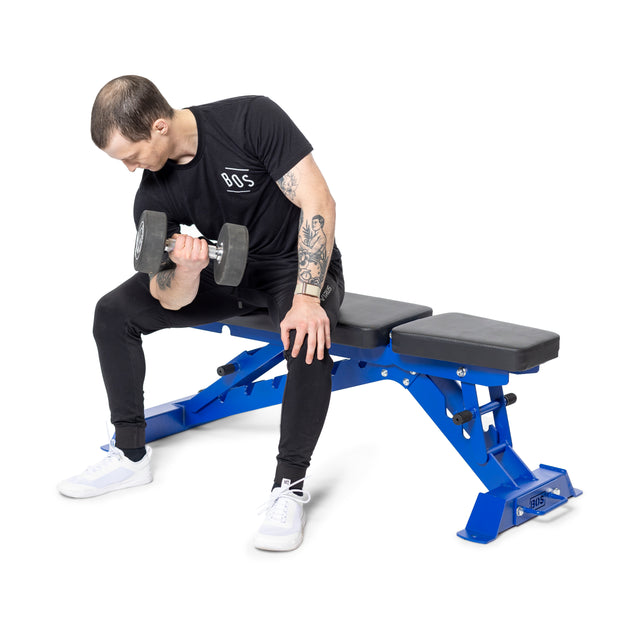 Seated on the Buzz-Saw Heavy-Duty Adjustable Bench by Bells of Steel, a person with short hair performs a bicep curl using a dumbbell. The 1,000lb capacity and adjustable back pad support their form. They wear a black t-shirt and pants with white sneakers.