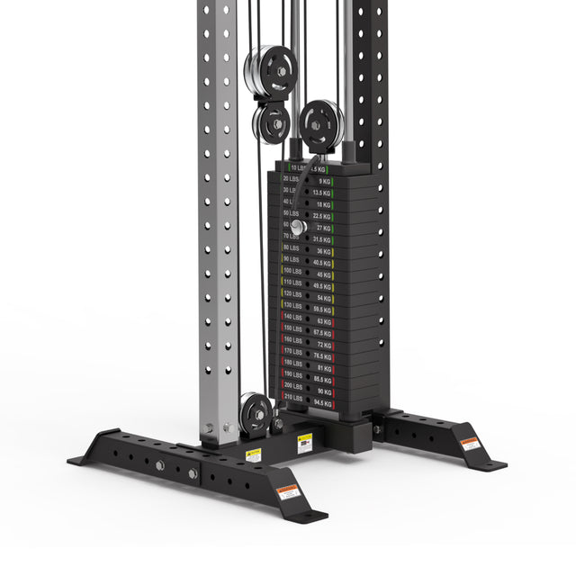 The image features a Bells of Steel Cable Tower in a gym. The weight stack shows weights labeled in pounds and kilograms, linked by pulleys within a sturdy metal frame. The base has adjustable holes for customization, providing versatile workouts with adjustable handles.