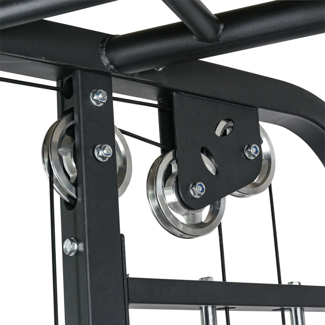 Close-up of the Bells of Steel Functional Trainer, a black metal fitness machine with a pulley system featuring three shiny metal wheels and tension cables. Sturdy bolts and brackets enhance its functionality, with versatile cable attachments and visible overhead pipes in the background.