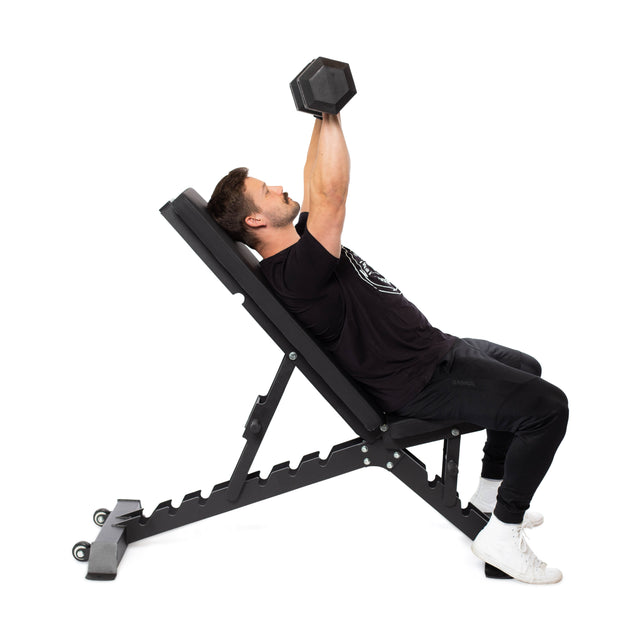 On a Buzz-Saw Heavy-Duty Adjustable Bench by Bells of Steel, a person reclines in an inclined position, lifting a dumbbell. They wear a black t-shirt and pants with white sneakers. The bench's adjustable back pad is set against a pristine white background.